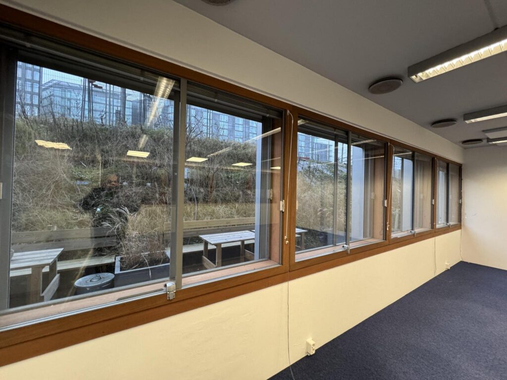 Interior office space with large windows overlooking the outdoor seating area and vegetation at De Ruijterkade.